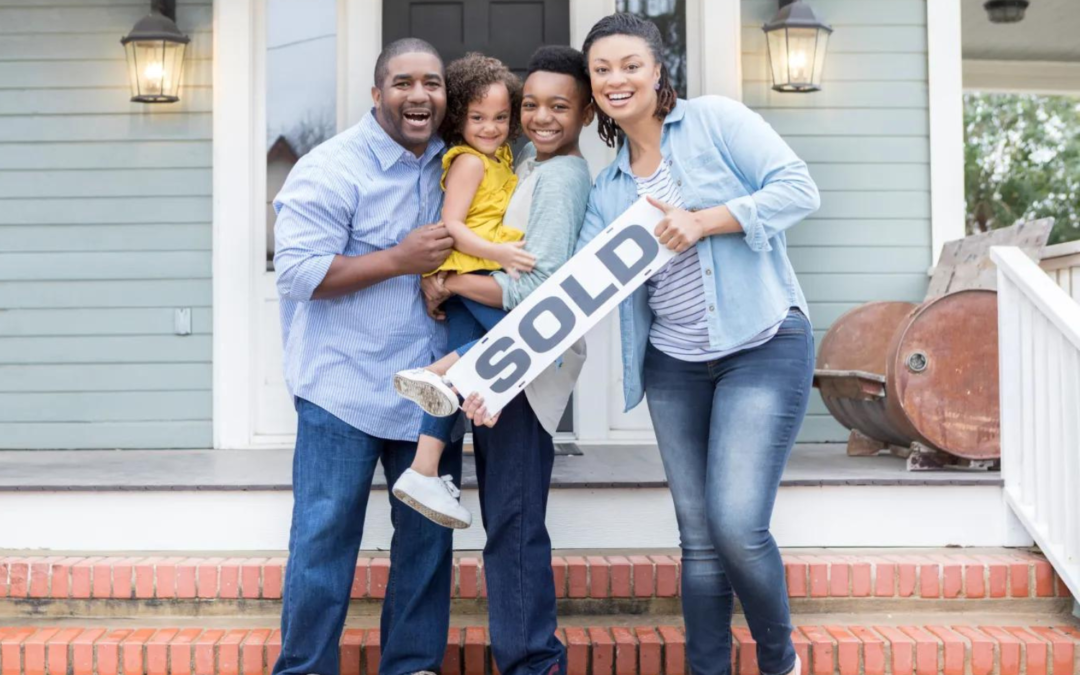 A happy couple standing in front of their new home with a "Sold" sign in Sioux Falls